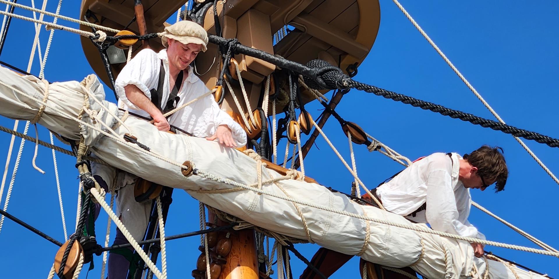 Two sailors working on a ships sail